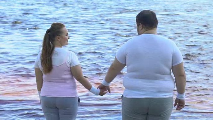 肥胖的男人牵着女朋友的手，夫妇享受着美丽的河景