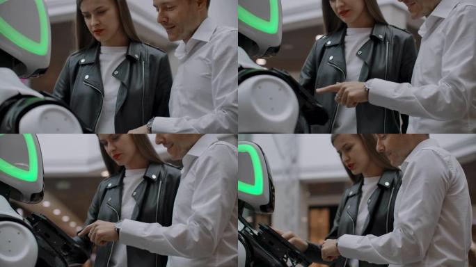 商场里的一男一女通过点击屏幕和微笑与机器人顾问互动。机器人机器人帮助人们。