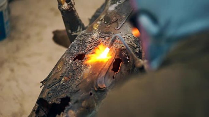 焊工在火花和烟雾的同时焊接钢雕塑和佛陀的修复细节。