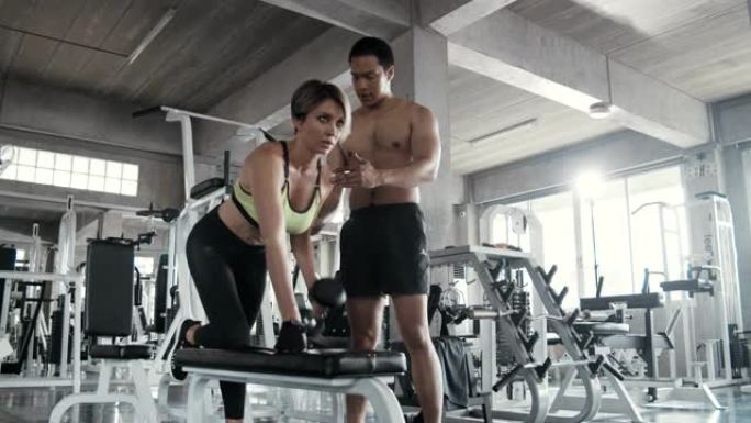女人在健身房与私人教练一起举重