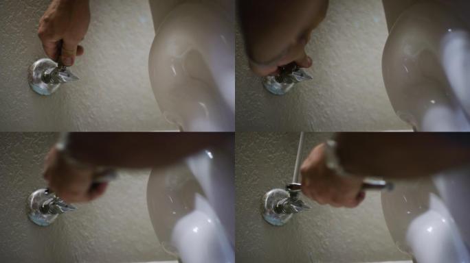 一名高加索修理工用手指和可调扳手将马桶软管连接到室内家庭浴室墙壁上的截止阀