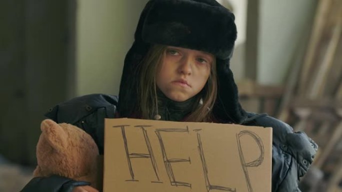 悲伤的无家可归的孩子拿着帮助纸板看着相机的肖像