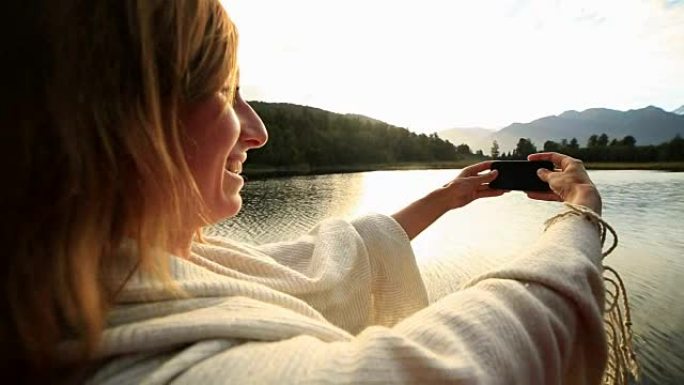 女人用手机拍摄山湖景观