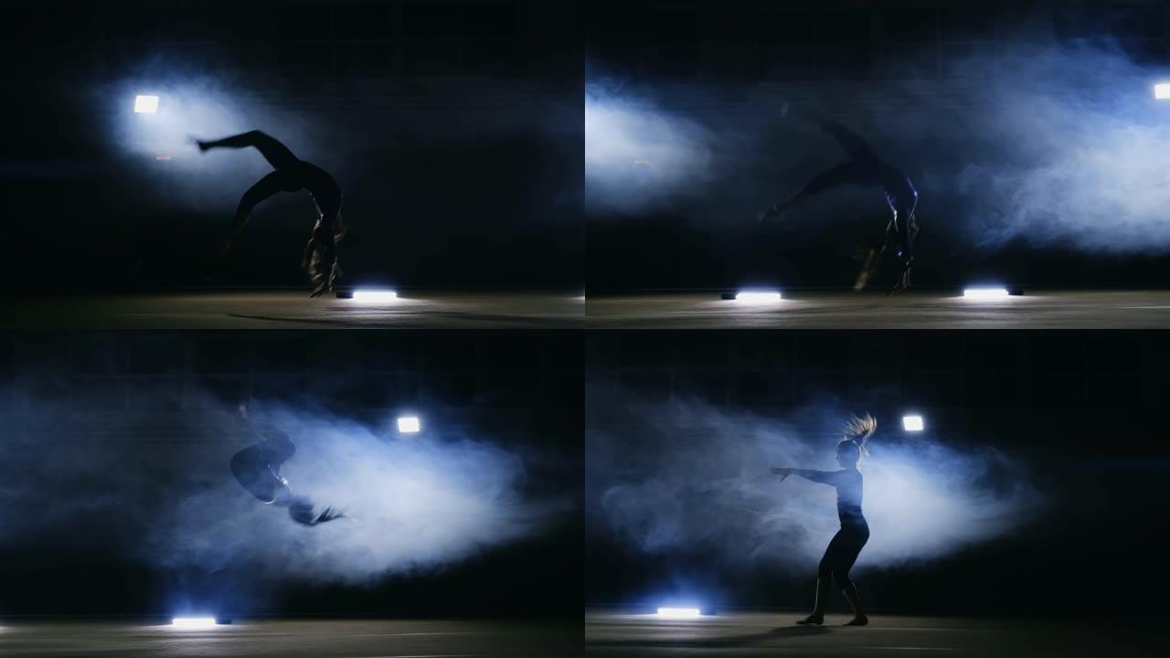 才华横溢的女孩体操运动员在烟雾中的灯光下以慢动作在体操地毯上进行翻转