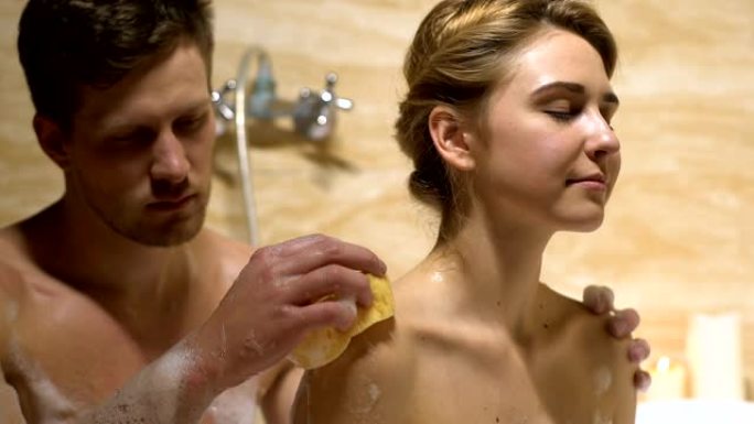 甜蜜的夫妇享受洗澡的时光，男人用海绵洗女人回来，浪漫