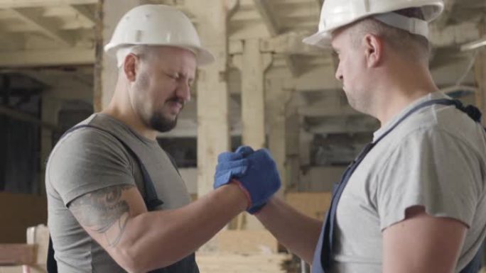 两名身穿白盔的白人强壮建筑商在施工现场握手。工人们指着 “是”，一个人离开了。
