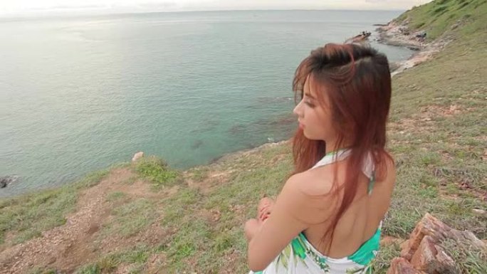 年轻的亚洲妇女坐在山崖和大海的背景上