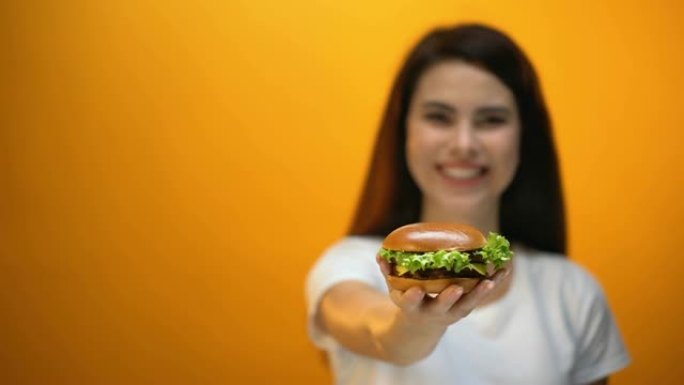 快乐女孩向相机展示汉堡包，快餐店满意的客户