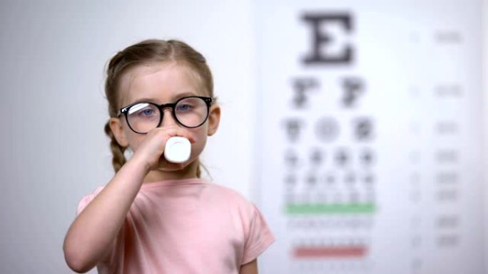 欢快的孩子在眼镜中喝美味的维生素糖浆以改善视力