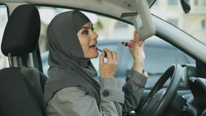 有吸引力的自信的穆斯林女士涂口红坐在车里，卖弄风情