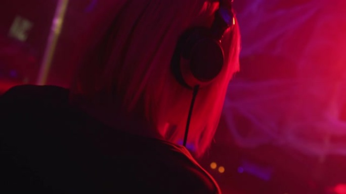 戴着耳机的女dj在夜总会工作，在派对灯光下随着音乐跳舞