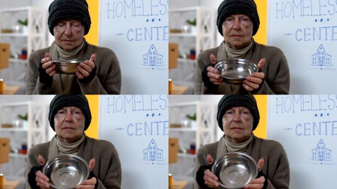 沮丧的饥饿无家可归的女性向镜头展示空盘子，贫穷