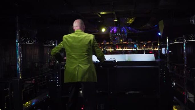 穿着绿色夹克的白人老人混合音乐和舞蹈的后视图。在夜总会工作的成熟男性DJ。活跃的老年人，生活方式，娱