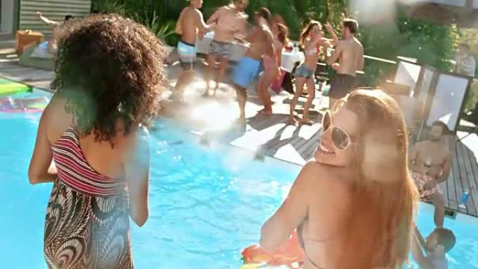 SLO MO两名年轻女子在泳池派对上与朋友一起笑着，用喷水枪将水射向镜头