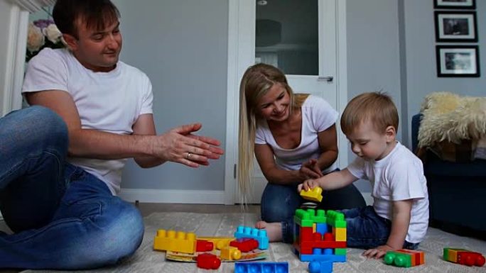 幸福的家庭爸爸妈妈和宝宝两年在明亮的客厅里玩塑料块。慢镜头拍摄幸福家庭