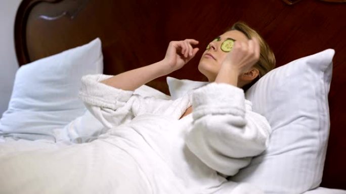 女人躺在床上，把黄瓜放在眼睛上，自然美容程序，更新