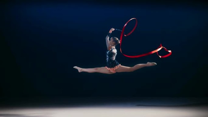SLO MO艺术体操运动员旋转红丝带并进行跳跃