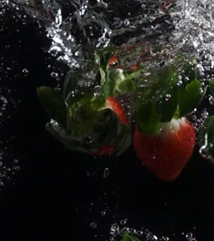 垂直慢动作: 草莓落入黑色背景下的淡水中