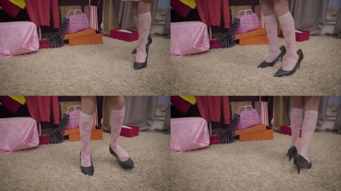 穿着粉红色袜子和成人高跟鞋的高加索小女孩的特写脚在室内柔软的地毯上行走。优雅的孩子梦想成为时尚模特。