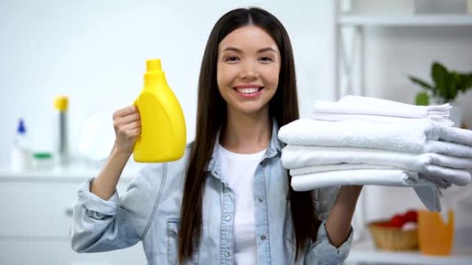 微笑的女人展示干净的毛巾和洗衣液，织物柔软剂