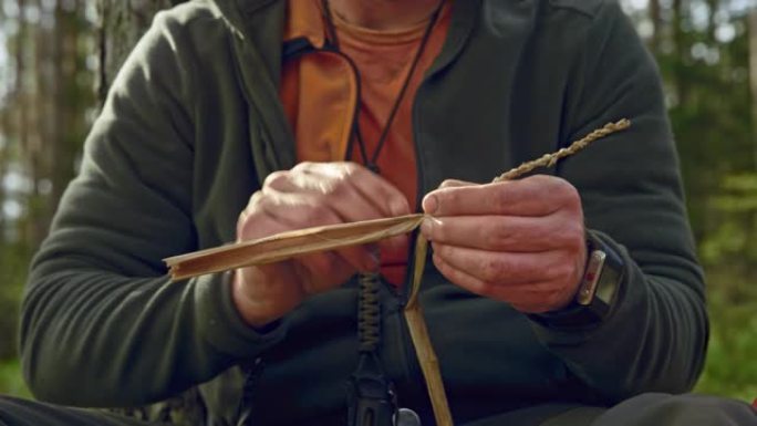 男性荒野生存专家在森林里用干草编织东西
