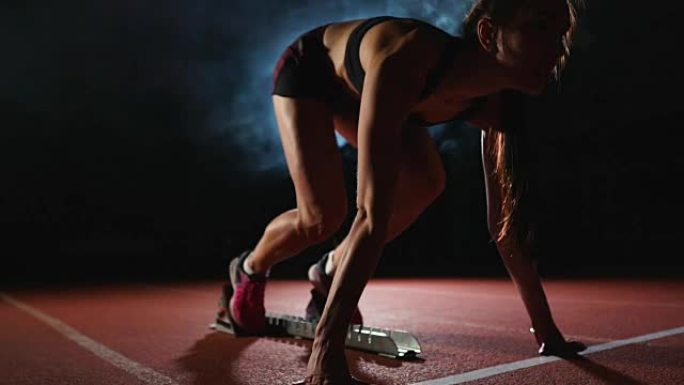 职业女运动员在黑暗的背景下，在体育场的跑道上，在黑暗的背景下，穿着运动鞋跑慢跑鞋的冲刺。特写