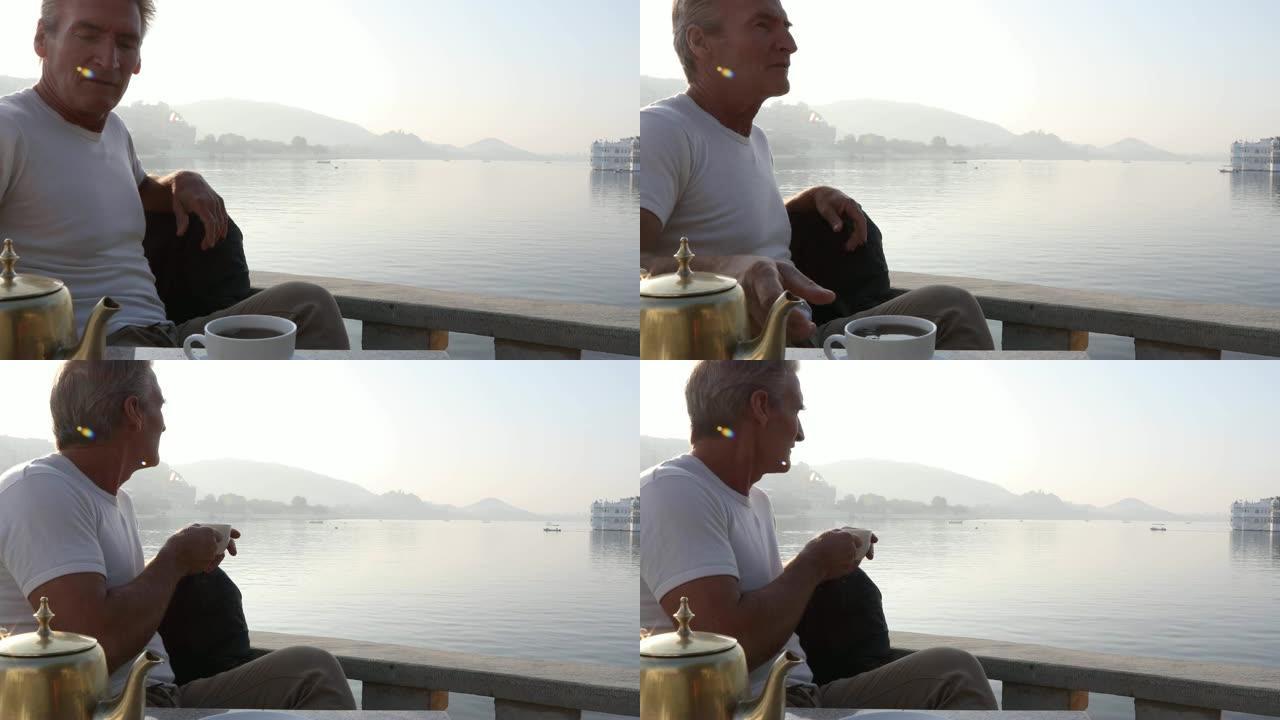 男人在日出时在湖岸上倒茶