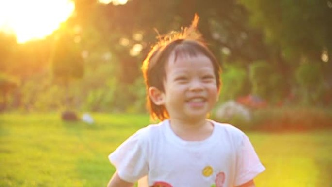 高清: 快乐的小男孩在日落背景下在公园跑步。