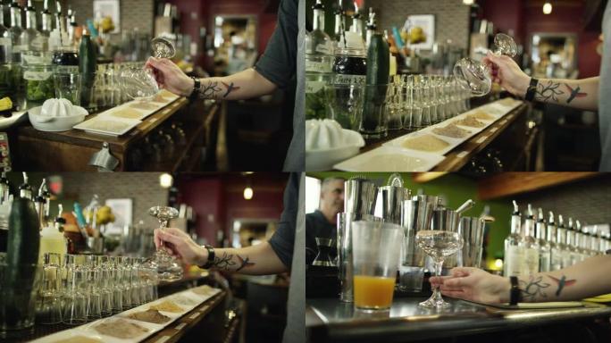 一位纹身的高加索女性调酒师将马提尼酒杯浸入几种不同的粉末中，以装饰轮辋，然后将其放在柜台上，同时在酒