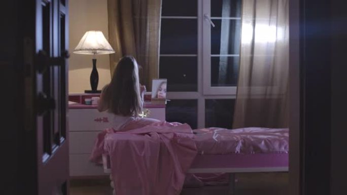 白人女学生坐在粉红色的床上洗完妆。可爱的长发孩子准备晚上在她的房间里睡觉。青春期，童年，休息。电影院