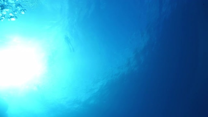 水下水肺潜水员在海洋表面附近的水下视图，并带有气泡