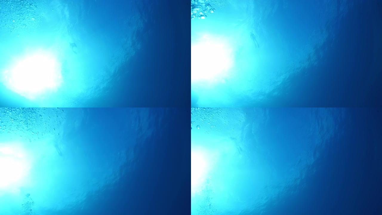 水下水肺潜水员在海洋表面附近的水下视图，并带有气泡