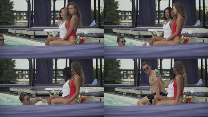 两位穿着比基尼的年轻漂亮女士在游泳池附近闲聊，有斗嘴的男人决定让她们开心
