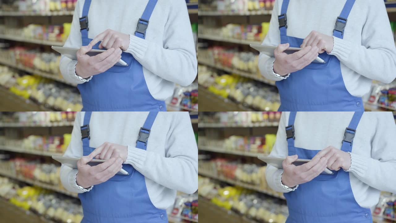 身穿制服的不知名白人男子站在杂货店使用平板电脑。无法识别的人在超市里扫屏检查各种商品。零售。商业，服