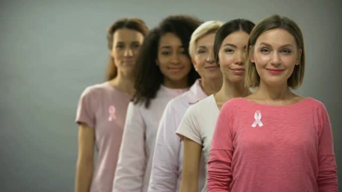 快乐的女人穿着粉色衬衫，系着乳腺癌丝带，站在队伍里