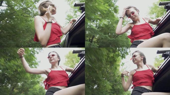 可爱的女孩俯身从车窗外挥动手臂户外风飘动女人头发女士在车里跳舞
