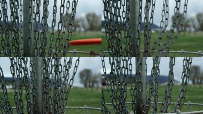 橙色圆盘高尔夫推杆在圆盘高尔夫球场 (飞盘高尔夫) 击中圆盘高尔夫篮的链条的特写镜头