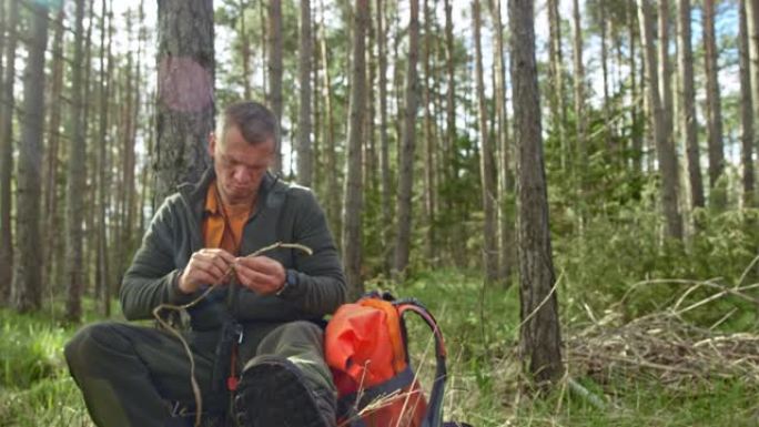 男性荒野生存专家坐在森林里用干草编织东西