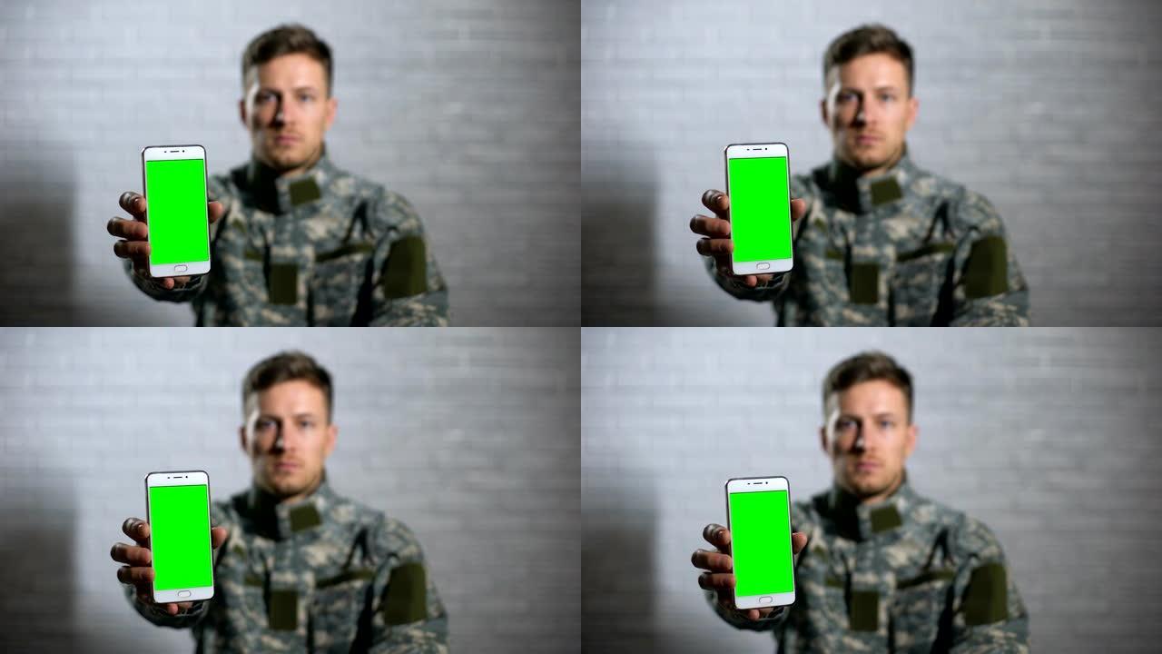 身着制服的男性士兵在摄像头前展示绿色屏幕的智能手机，应用程序