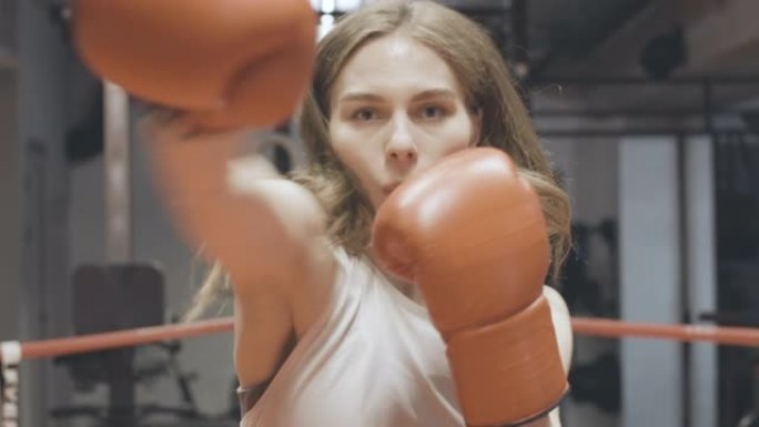 美丽的女拳击手拳击相机肖像。迷人的年轻苗条的高加索女人在拳击场上的健身房里挥拳的特写镜头。性别平等概