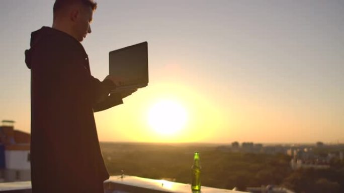 一个程序员带着笔记本电脑坐在屋顶上，在日落时分写代码。远程工作的自由职业者。自由的工作。日落时分，我