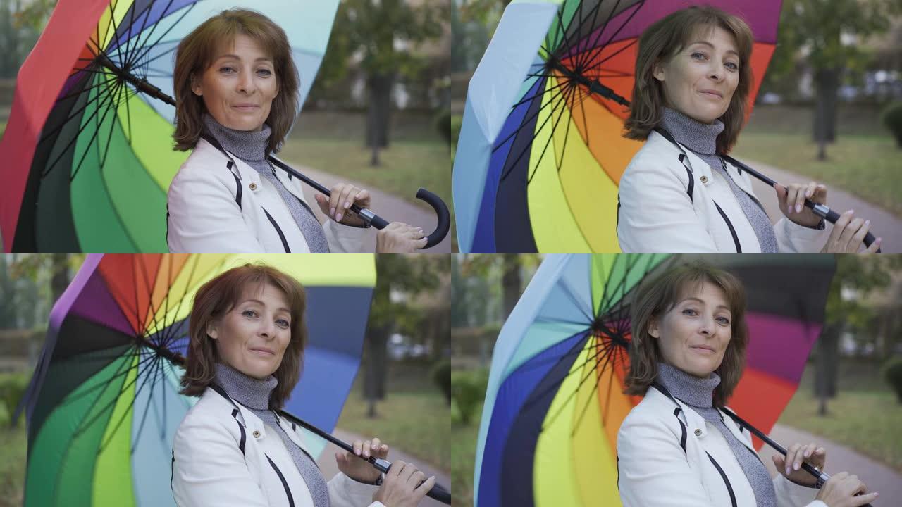 自信的高加索女人旋转着多色的雨伞，微笑着。
