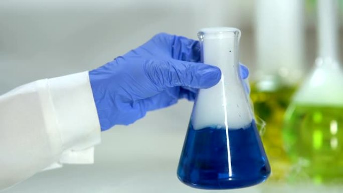 实验室工作人员戴着手套，用蓝色沸腾液体搅拌烧瓶，药理学