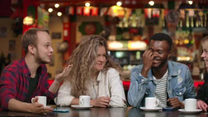 一个穿着衬衫的男人向朋友讲了一个故事，两个女孩和一个非洲裔美国人正在听和笑。一群朋友一起度过时光。学