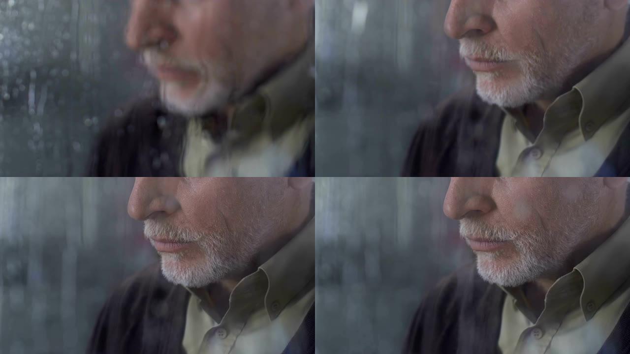 成熟的孤独男人叹息沉重地站在下雨的窗户旁，向外看