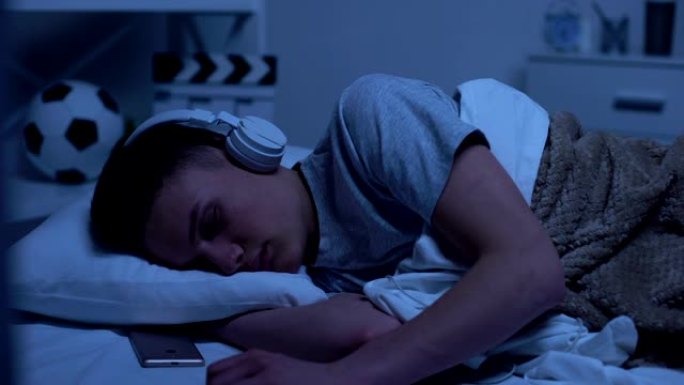 男十几岁的男孩戴着耳机睡着了，过度劳累的学生放松