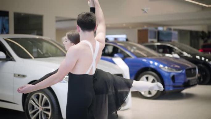 年轻美丽的高加索女人在男人的支持下踮起脚尖旋转。专业芭蕾舞演员在汽车陈列室跳舞。优雅，艺术，经典舞蹈