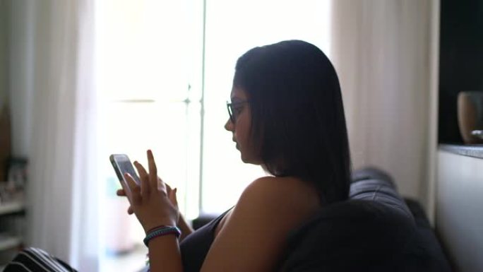 年轻女子在家中坐在沙发上使用智能手机