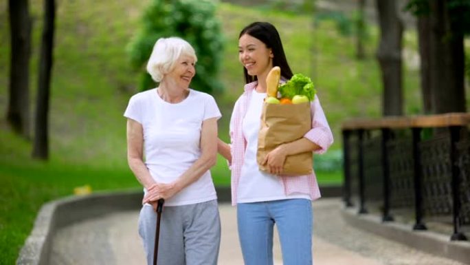 孙女带食物给老年女病人，在医院公园散步