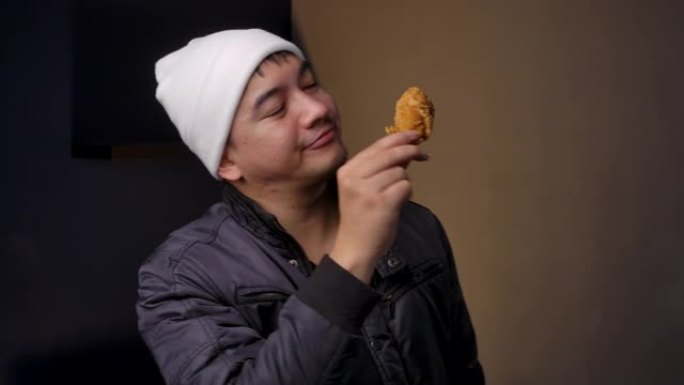 4k镜头青少年穿着冬装，他拿着炸鸡腿，他正在吃美味的炸鸡。